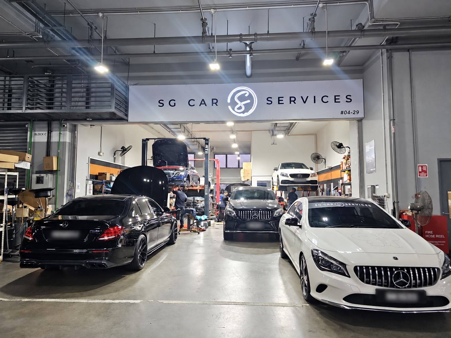 The SG Car Services workshop at Carros Centre, with cars on ramps under the workshop signage